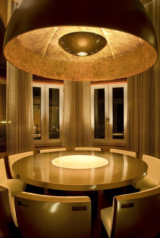 The Taj Mahal Tower, Mumbai Hotel Bagian luar foto The photo shows a modern dining room with a round table at the center. The table has a glossy surface and features a circular illuminated section in the middle. Surrounding the table are sleek, contemporary chairs. The room has large windows dressed 